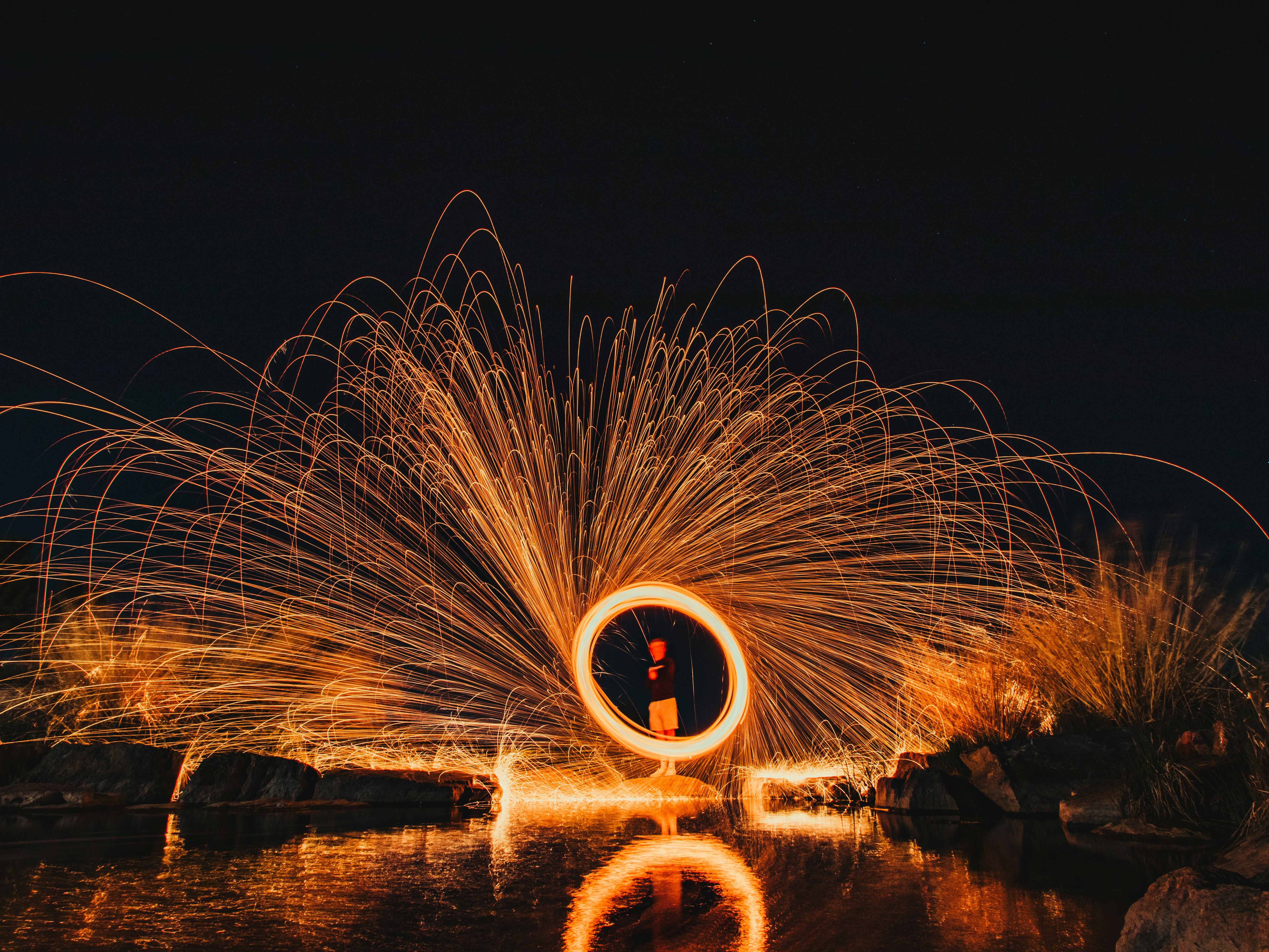 steel wool photography of man standing on the beach during night time